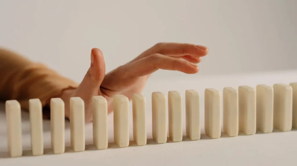 A hand interrupting a line of upright blocks, interrupting a chain reaction